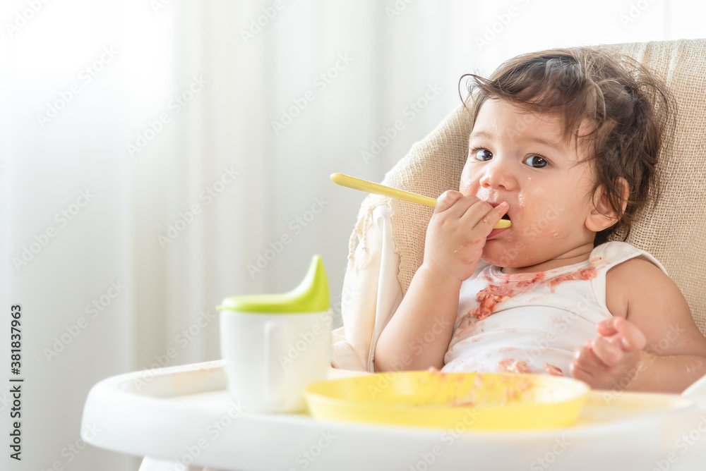 Messy baby girl eating cake. Lovely infant girl holding a spoon, enjoying eating cake. Messy baby girl eating cake. Lovely infant girl holding a spoon, enjoying eating cake.