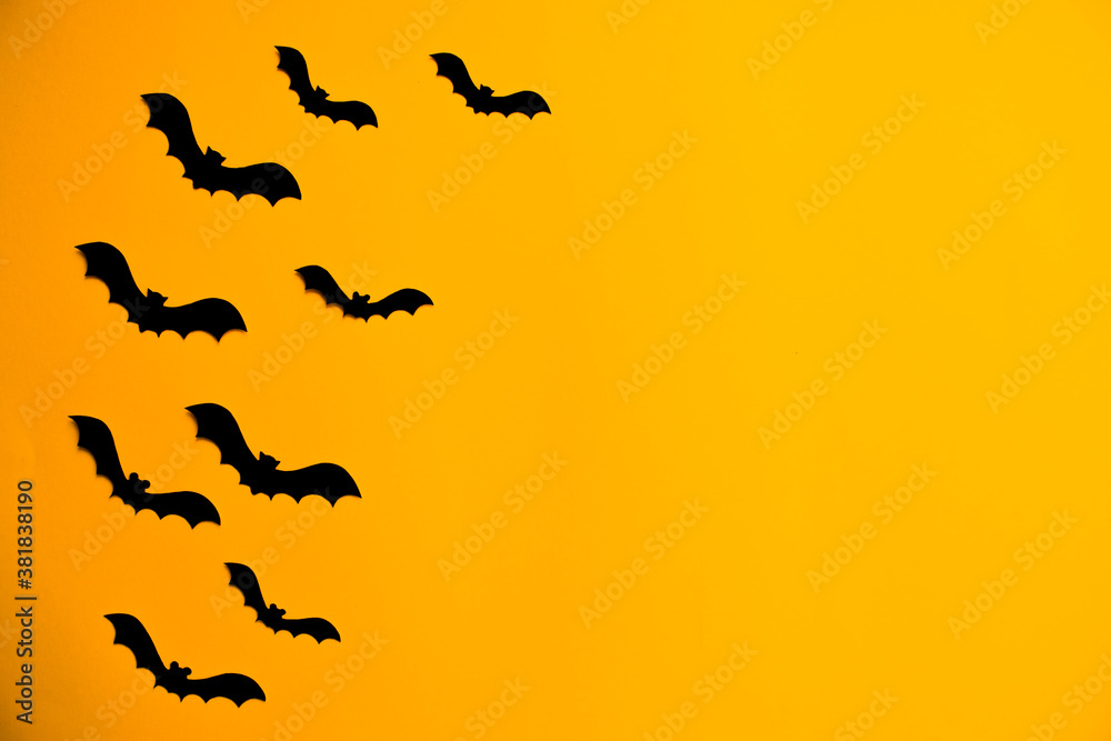 Silhouettes of black bats made of paper on orange background. Halloween greeting template with copy space. Flat lay for your design.
