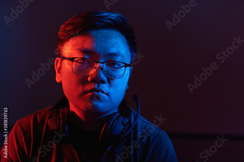 Portrait of Asian young hacker in eyeglasses and in headphones doing his criminal work in dark room © AnnaStills