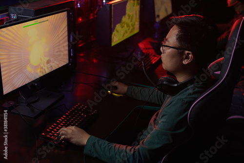 Asian young gamer in eyeglasses looking at computer monitor he concentrating on his game in dark computer club © AnnaStills