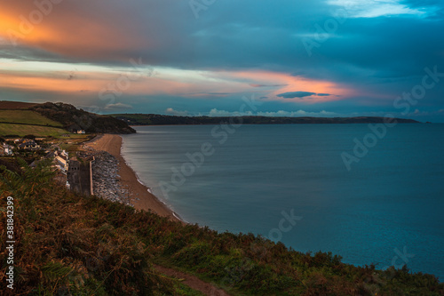 Beesands beach and village pictured from hills above looking down at the sea and beach. Image taken at the end of golden hour showing lots of colours in the sky and a calm blue sea