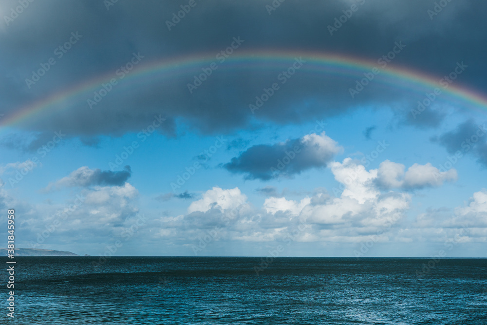 A big bold rainbow over the sea with cloudy blue sky behind it. Copy space available
