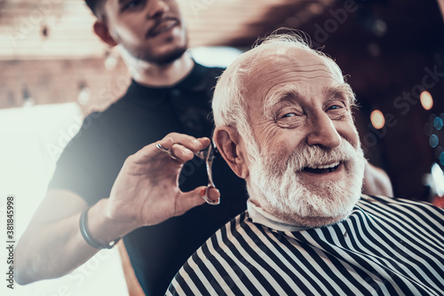 Old man looks at camera while master cuts his hair