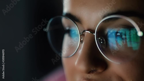 Young woman at home during quarantine. Close up girl's face looking on screen with its reflecting. Watching video or movie late at night.