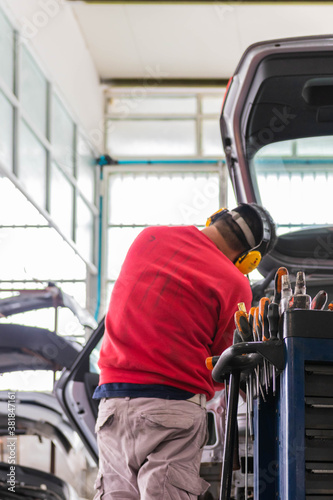 Expert senior mechanic repairing a car after a street crash. Details and focus on metal parts and electric wires. Blurred background, natural light. Occupation and job concept.