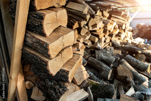 Chopped firewood storage under shed and oak wooden tree logs prepared for chopping and cutting at home backyard. Woodshed store at house yard.Timber material for heating alternative renewable energy