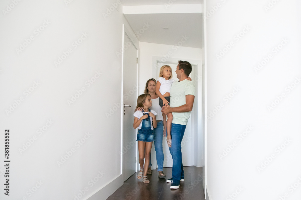 Happy family going through corridor of their new house. Mom, dad and children walking near doors and talking. Father holding little daughter in hands. Mortgage, relocation and moving day concept Happy family going through corridor of their new house. Mom, dad and children walking near doors and talking. Father holding little daughter in hands. Mortgage, relocation and moving day concept