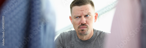 Man with thoughtful look selects clothes on hanger. Modern and stylish clothing store concept
