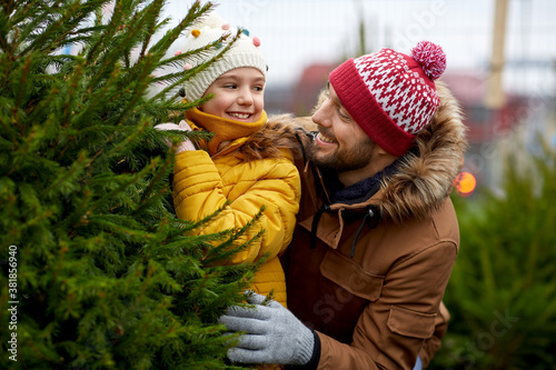 family, winter holidays and people concept - happy father and little daughter choosing christmas tree at street market