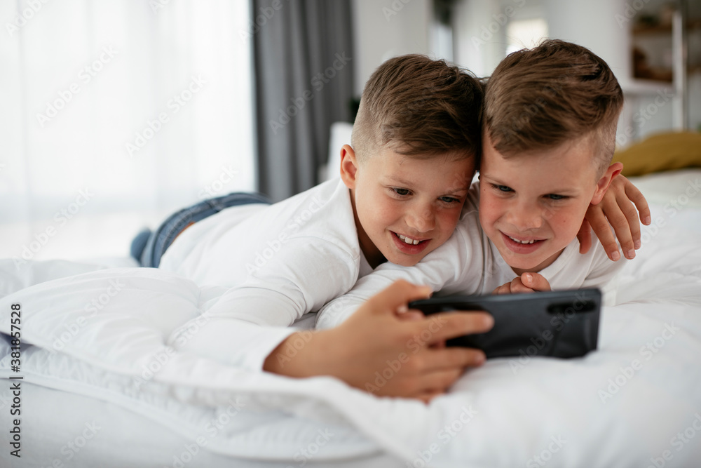 Two little brothers are playing games on the phone. Beautiful boys enjoying at home.. Two little brothers are playing games on the phone. Beautiful boys enjoying at home..