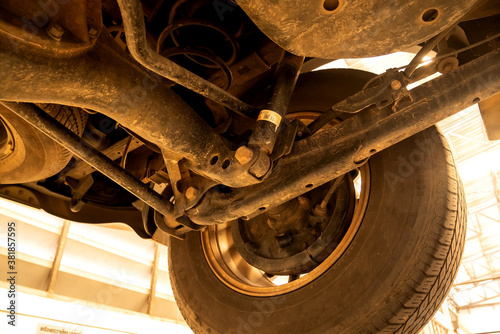 Under old car closeup rear wheel axle suspension and exhaust chamber silencer muffler dirty fix repair in garage.