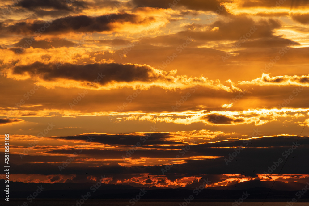 Fototapeta premium a golden image of the sun setting behind mountains and clouds in southern Spain 