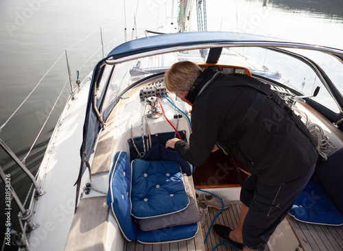 Senior man arranging the ropes to run up the sail while sailing on the sea wearing a life jacket