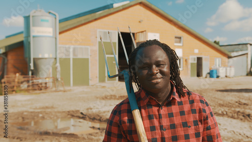 Young african farmerholding fork over the soulder and smiling in front of the silo system . High quality photo photo