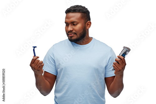 shaving, grooming and people concept - young african american man choosing between manual razor blade and trimmer over white background