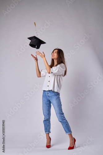 Smiling caucasian girl is throwing up her graduate hat. Beautiful girl dressed in jeans and white shirt isolated on white background. photo