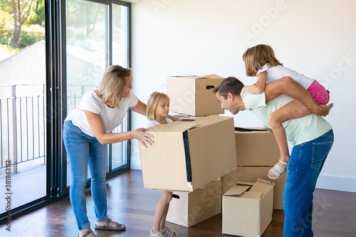 Happy parents and kids celebrating apartment buying, opening boxes and having fun in their new flat. Real estate purchase concept