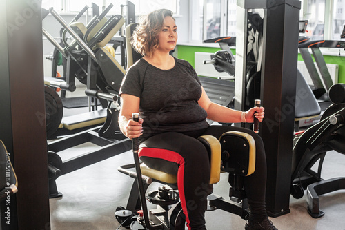 Slika na platnu Fat woman fights overweight in the gym, doing heavy fitness exercises for future strong body
