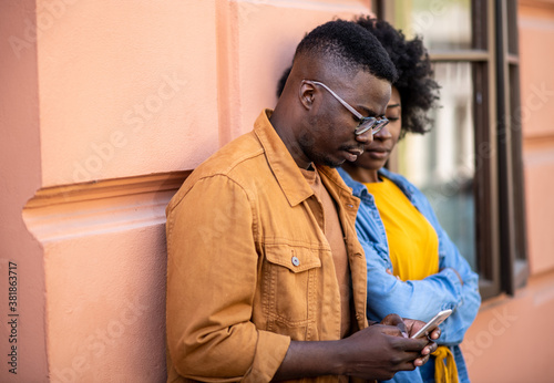 Happy young couple outdoors, spending time together, he holding a smart phone and looking at it