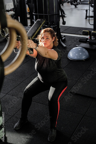 Fototapeta Naklejka Na Ścianę i Meble -  Fat woman fights overweight in the gym, doing heavy fitness exercises for future strong body. Obese person workout with sport equipment