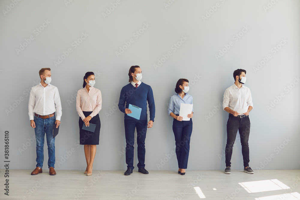 Obraz premium Job seekers in face masks waiting for job interview standing in corridor keeping safe distance