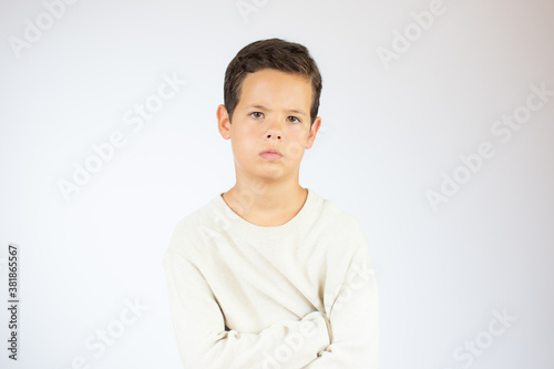 Portrait of a serious or calm caucasian boy with crossed arms wearing white sweater on white background