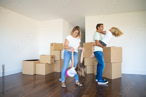 Joyful parents and kids enjoying new home, dancing and having fun near heaps of boxes in empty room. Full length. Apartment buying concept
