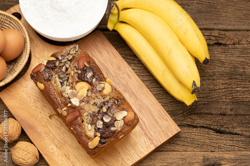 Banana cakes are placed on a wooden tray on a wooden table, with bananas, eggs, flour as background. Top view picture.