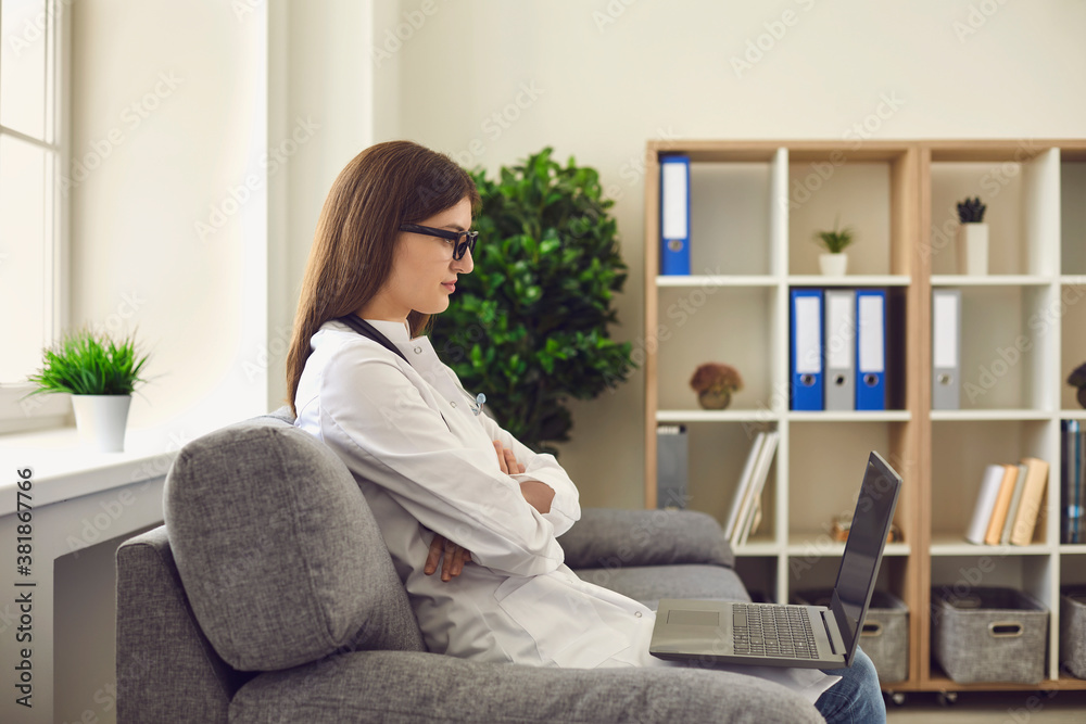 Woman doctor therapist sitting in medical clinic and looking at laptop during online meeting Woman doctor therapist sitting in medical clinic and looking at laptop during online meeting