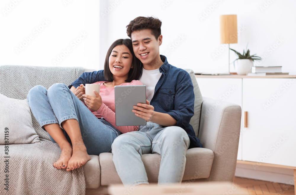 Asian Couple Using Digital Tablet Sitting On Sofa At Home Asian Couple Using Digital Tablet Sitting On Sofa At Home