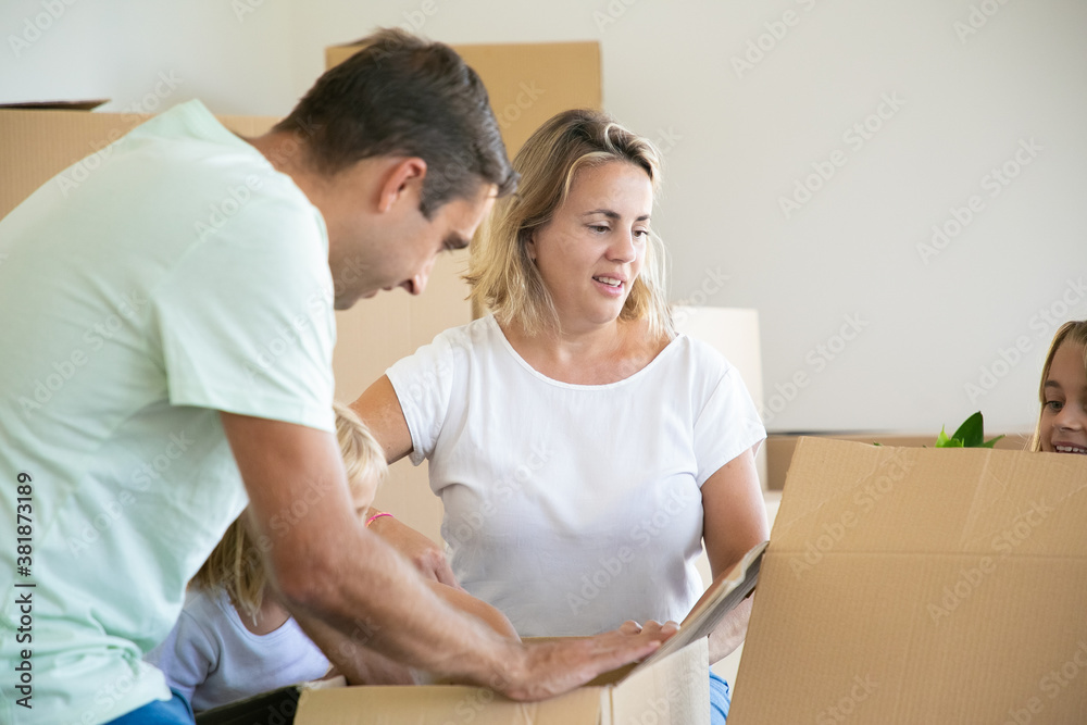 Family couple and kids unpacking things in new apartment, sitting on floor and opening boxes. House buying or moving concept Family couple and kids unpacking things in new apartment, sitting on floor and opening boxes. House buying or moving concept