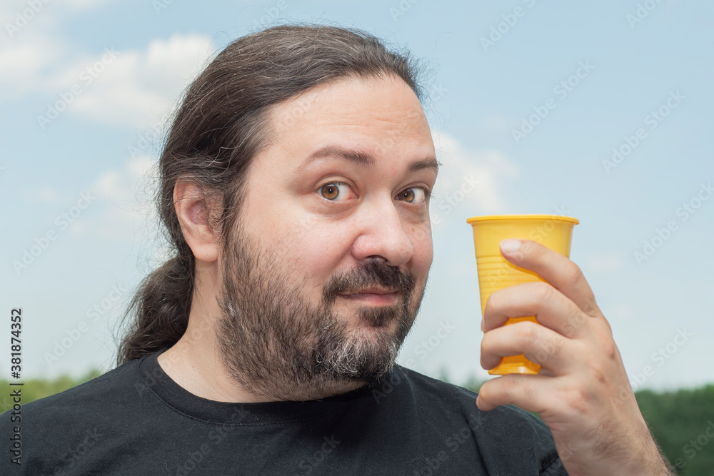 Fototapeta premium An adult man with a beard shows an empty, yellow plastic cup. Man on a light background.