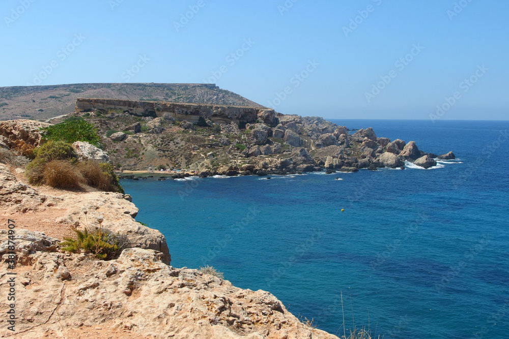 Golden bay beach on Malta island with beautiful blue sea water and rocky coastline in bright sunny day