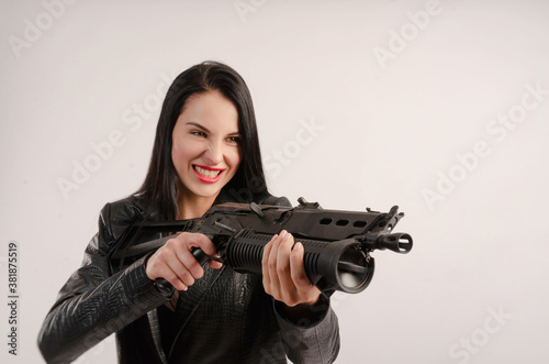 a brunette woman poses in a leather jacket with her back against a white background with a gun