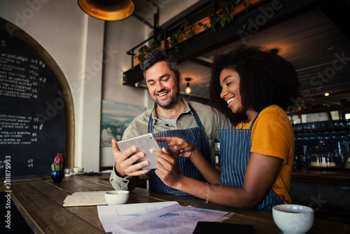 Manager and waitress laughing at designs on digital tablet standing with hot coffee in cafe 