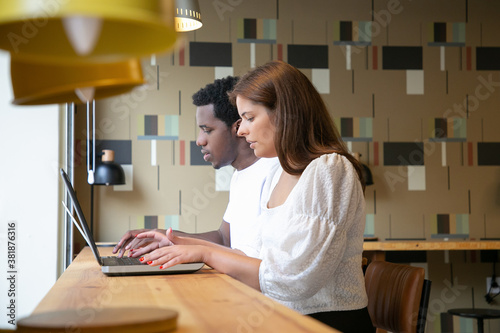 Multiethnic designers sitting together and working on laptops in coworking space. Concentrated content colleagues looking at screen and creating design. Communication and digital technology concept