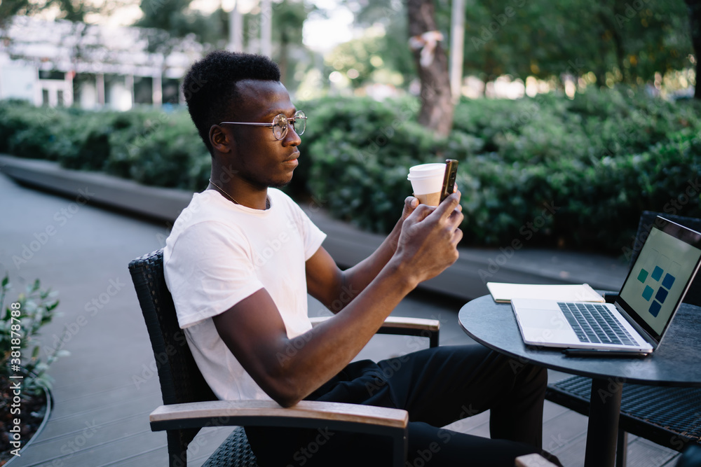 Fototapeta premium Black man with coffee browsing smartphone in street cafe