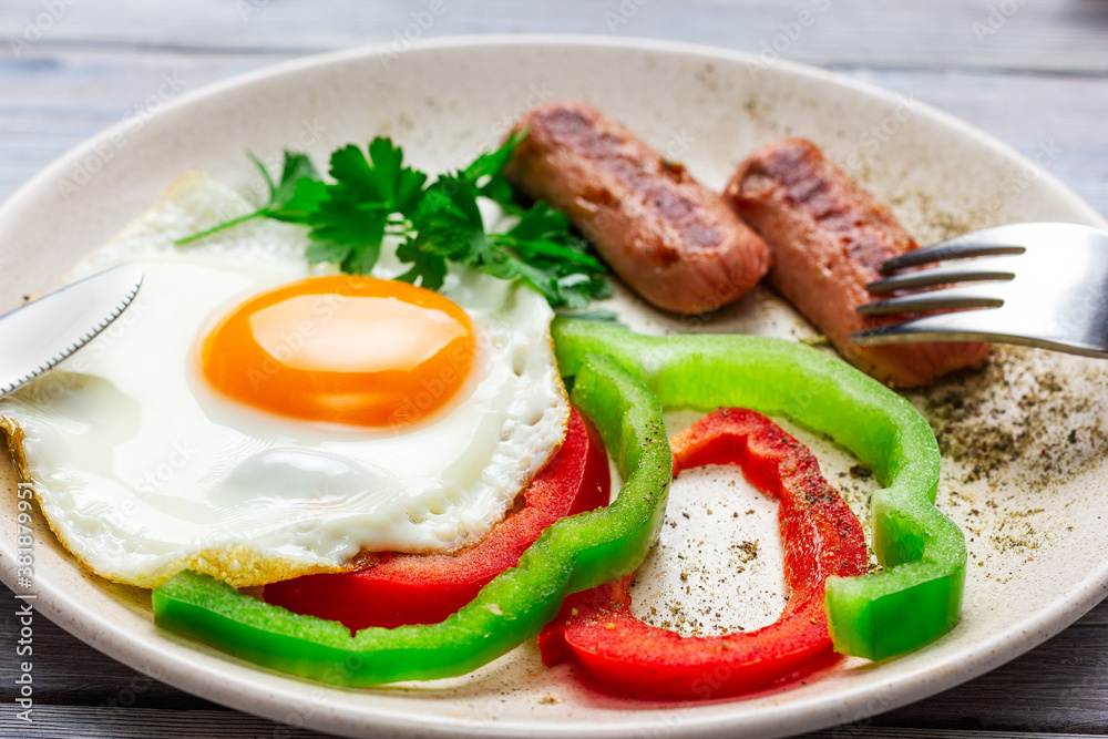 sunny side up. Fried eggs with sausages and vegetables on a light wooden table. sunny side up. Fried eggs with sausages and vegetables on a light wooden table.