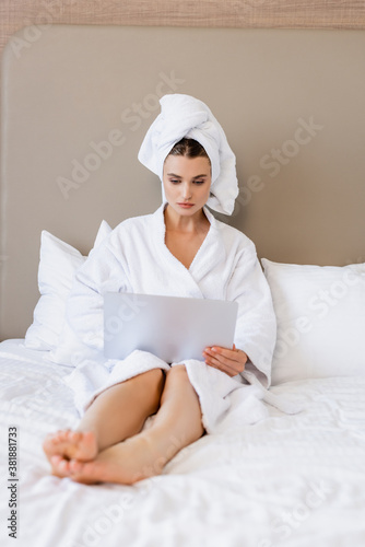 selective focus of barefoot woman in bathrobe and towel using laptop on bed