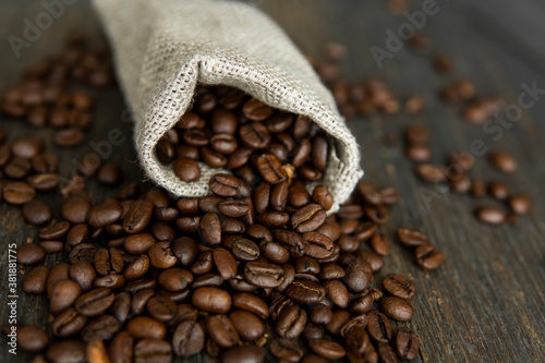 Coffee beans scattered from a linen bag on a wooden table. Fresh arabica coffee beans on linen textile. © Volodymyr