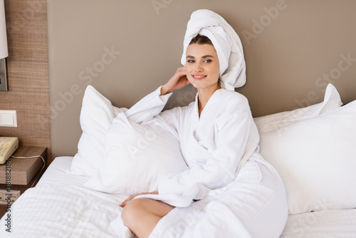 pleased woman in towel and white bathrobe lying on bed in hotel room