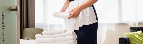 cropped view of maid in apron holding clean towel in hotel room, panoramic shot