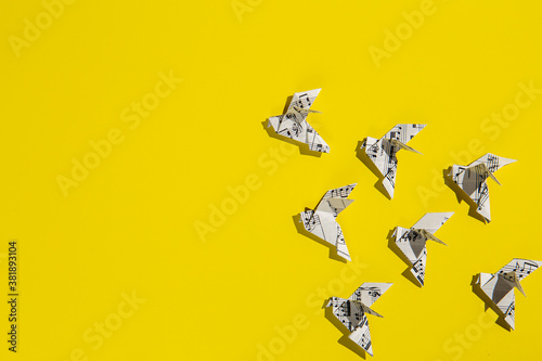Flock of flying origami doves on yellow background. Origami birds of music paper. Concept of festive music postcard.