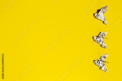 Flying origami doves on yellow background. Origami birds from music paper. Concept of festive music postcard.