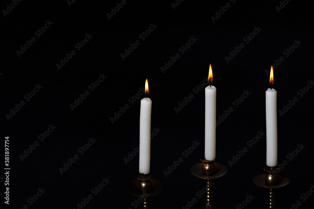 Antique copper candlestick with three burning white candles isolated on black background, copy space, close-up Antique copper candlestick with three burning white candles isolated on black background, copy space, close-up