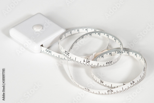 Small white tape measure for home use, with lock button, uncoiled to about 30 inches, on white background
