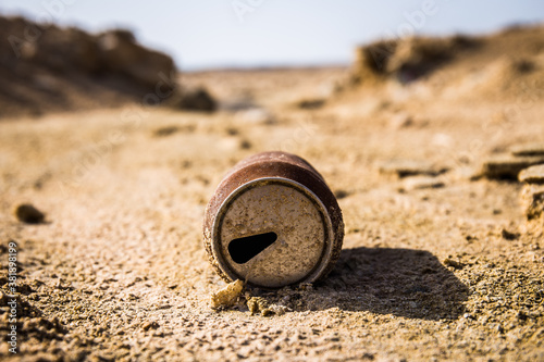 Empty old soda can laying in the desert sand with hills in back
