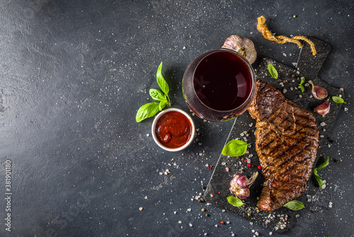 Grilled roasted meat beef steak on black background, with wine, ketchup sauce, herbs and spices, top view.