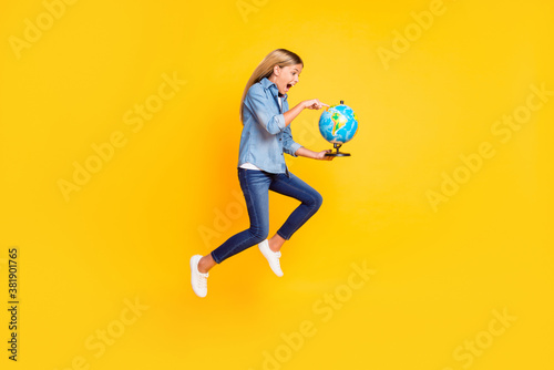 Full length body size photo of amazed jumping high schoolgirl keeping globe pointing on continent shouting amazed isolated on bright yellow color background © deagreez