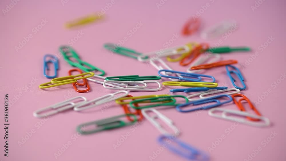 colored paper clips fall on the pink table. school supplies. paper clips close up colored paper clips fall on the pink table. school supplies. paper clips close up